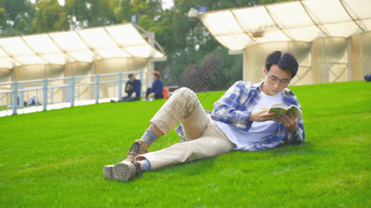 穿羽绒服男孩穿格子衫的男生在草地看书GIF高清图片
