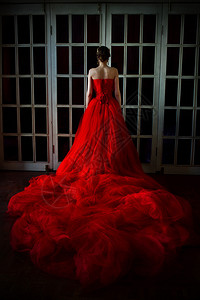 穿长红色裙子的漂亮女人穿着皇冠站在旧后门附近背景图片