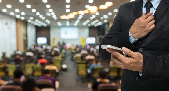 商人在会议厅或会议室的抽象模糊照片上使用智能手机图片