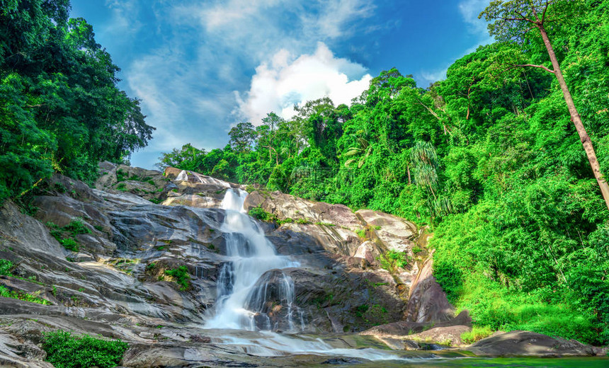 在山的美丽的瀑布与蓝天和白色积云热带绿树林中的瀑布瀑布在丛林中流动自然抽象背图片