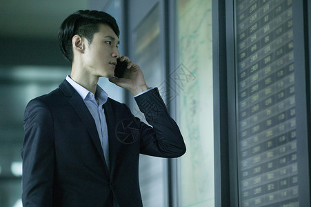 到达成功的路径商务男士在机场时间表前用手机通话背景