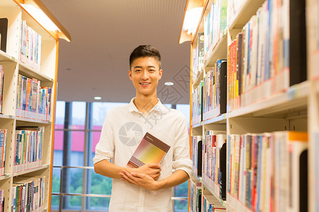 站在图书馆书架旁看书的帅气男同学选书高清图片素材