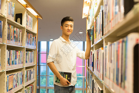 男生在图书馆书架旁选看图书图片