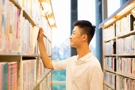 男生在图书馆书架旁选看图书教育高清图片素材