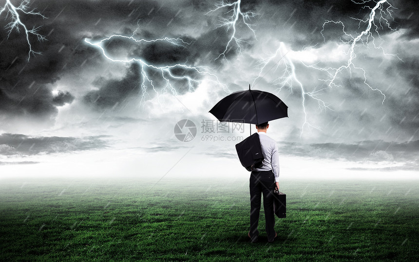 打伞商务人站在打雷下雨的草坪上