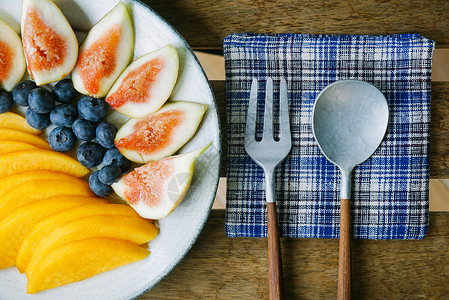 一盘无花果、蓝莓、黄桃和叉子勺子图片