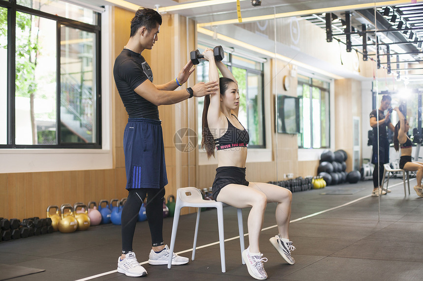 男教练在健身房给女性练习力量图片