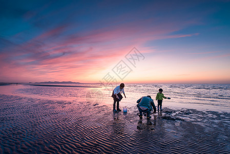 儿童海滩玩耍夕阳海滩上赶海的一家三口背景