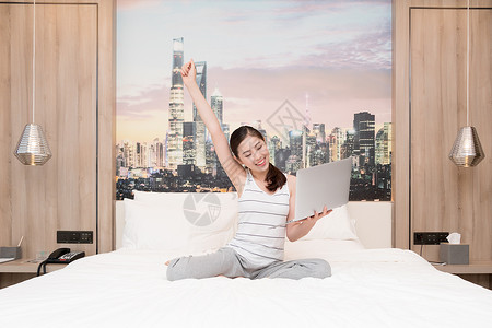 温馨笑脸年轻女性在床上玩电脑背景