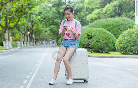 小清新开学季校园女生坐旅行箱上看手机背景