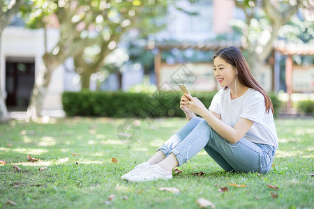 学生音乐素材坐在校园草坪上玩手机的女生背景