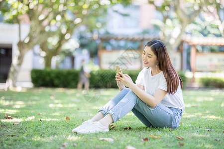 坐在校园草坪上玩手机的女生高清图片