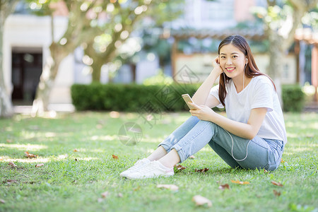 学生音乐素材坐在校园草坪上玩手机的女生背景