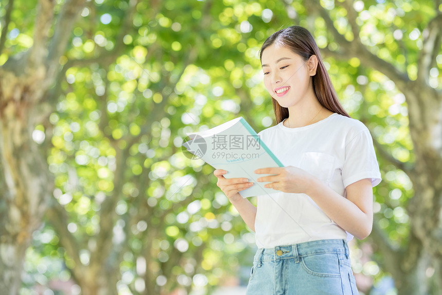 校园林荫道上微笑看书的学生图片