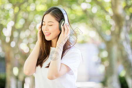 树林下戴耳机听音乐的甜美女生图片