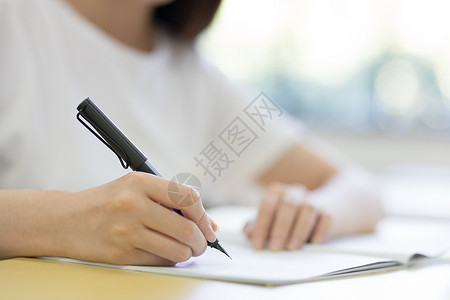 两位女学生教室手拿钢笔写字特写背景