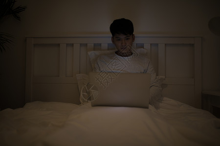 睡前坐在床上玩电脑打电脑的男子高清图片
