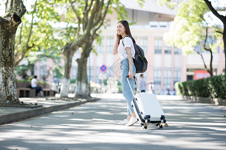 学校里拉着行李箱背书包的女生背景图片