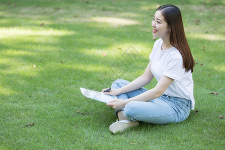 拿着课本坐在草坪上看书的大学生图片