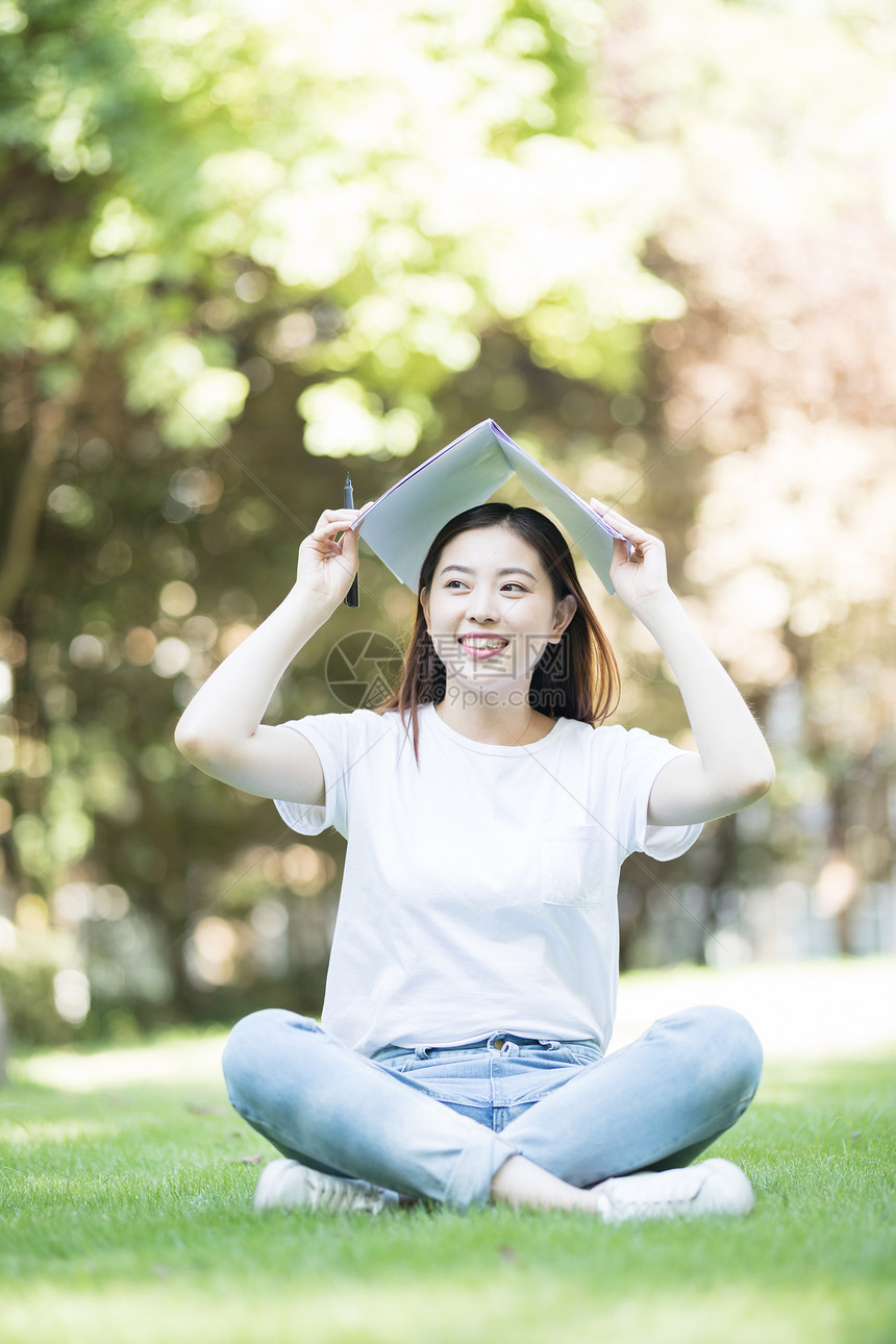 拿着课本坐在草坪上看书的大学生图片