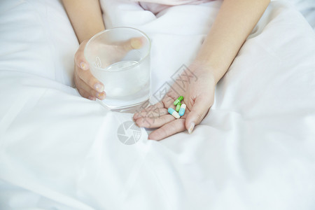 床上喝水在床上吃药的女性手部特写背景