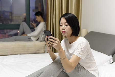 女子在床上玩手机和男子冷战高清图片