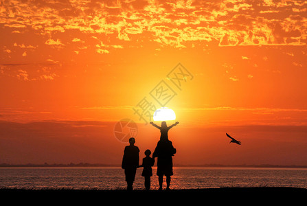 海边玩耍的孩子夕阳下家庭剪影设计图片