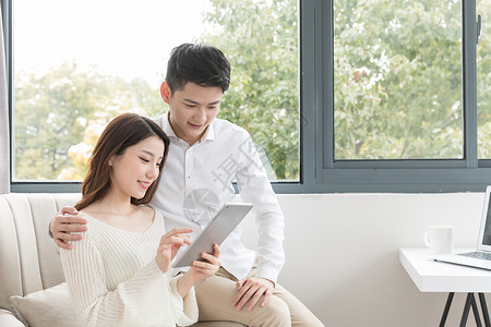 情侣看电脑年轻夫妻幸福地坐在沙发上看平板电脑背景
