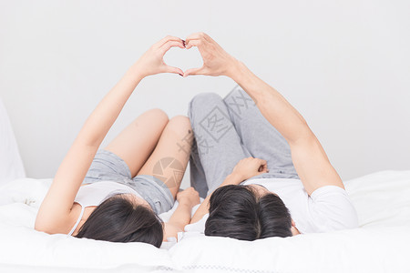 亚洲浪漫女孩年轻夫妻躺床上比心背景