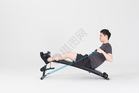 坐在运动器械上拉阻力带的健身男性背景图片