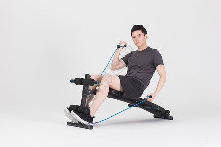 坐在运动器械上拉阻力带的健身男性背景图片
