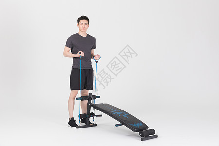 站在仰卧板旁拉阻力带的健身男性背景图片
