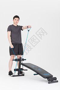 站在仰卧板旁拉阻力带的健身男性背景图片
