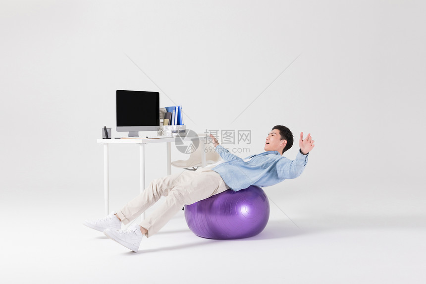 年轻职员坐在瑜伽球上锻炼图片