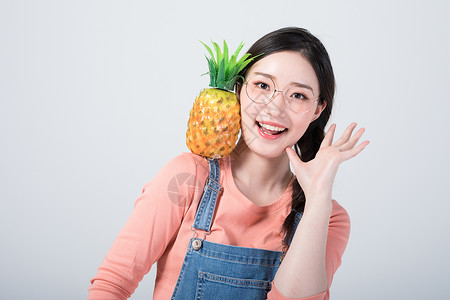 水果笑脸年轻美女手拿菠萝拍照背景