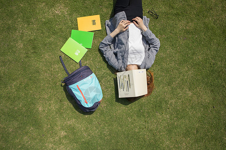 女学生躺在大学草坪上看书教育高清图片素材