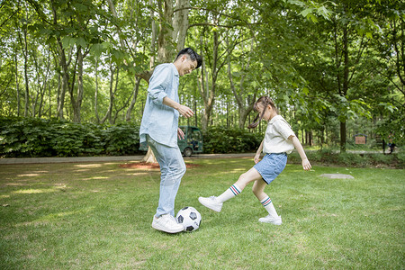 爸爸和女儿在草坪上踢足球背景图片