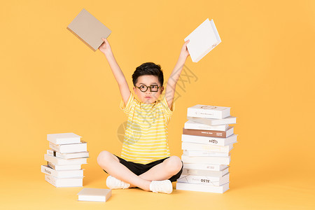 拿着书本坐在书旁的快乐男孩背景图片