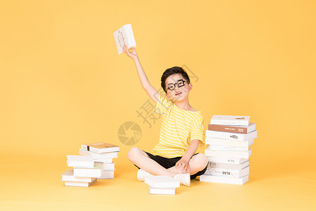 拿着书本坐在书旁的快乐男孩图片拿着书本坐在书旁的快乐男孩背景
