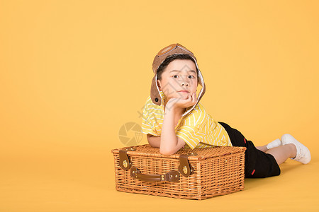 举着柠檬的男孩趴在行李箱上戴着飞行帽的小朋友背景