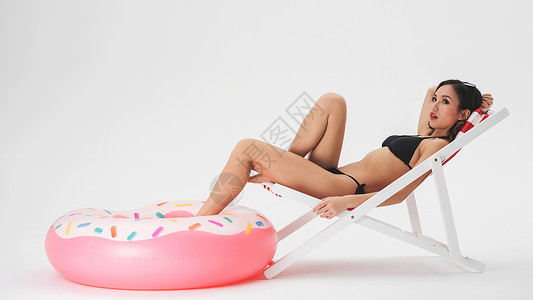 泳装美女坐在沙滩椅上与泳圈背景图片