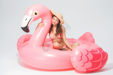 穿粉色比基尼的可爱卖女坐在火烈鸟游泳圈背景图片