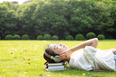 可爱女孩写字板青春学生躺草地上听音乐背景