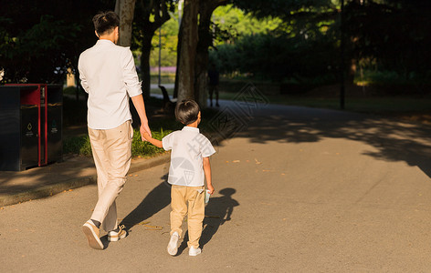 走路吃瓜的男孩公园里牵手散步父子背影背景