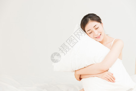 年轻女性床上抱着枕头放松背景图片