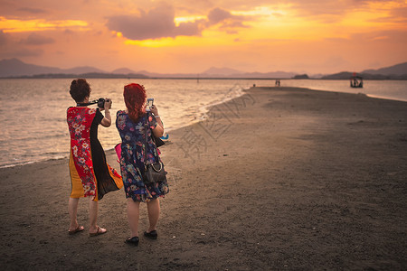 广东惠东盐洲岛海岸夕阳晚霞下拍照的游人背景图片