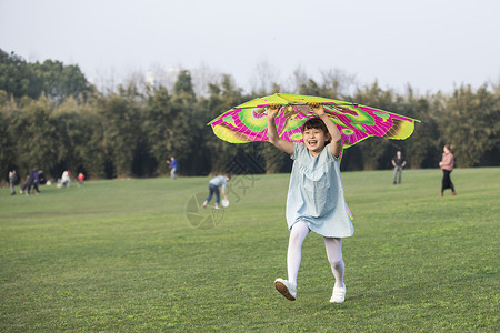 小女孩拿着风筝在草坪上奔跑背景图片
