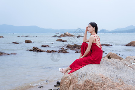 深圳较场尾海边礁石上的红衣少女侧影背景图片