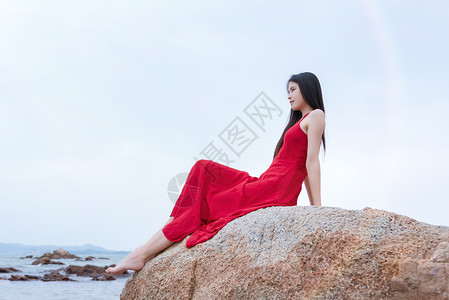 坐在深圳较场尾海边礁石上的红裙子少女高清图片