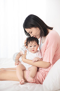 妈妈抱着小女孩妈妈在床上逗宝宝玩背景